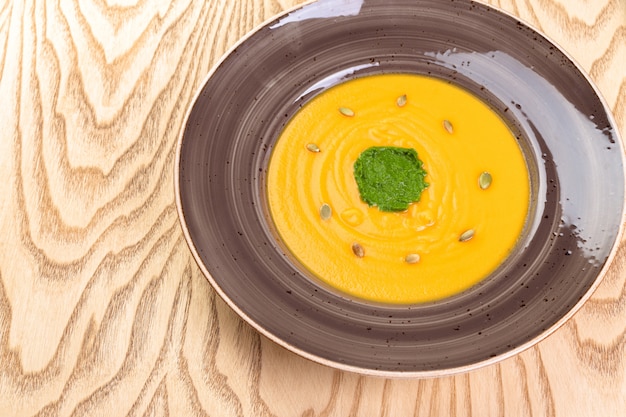 Bowl of pumpkin soup on rustic wooden background.