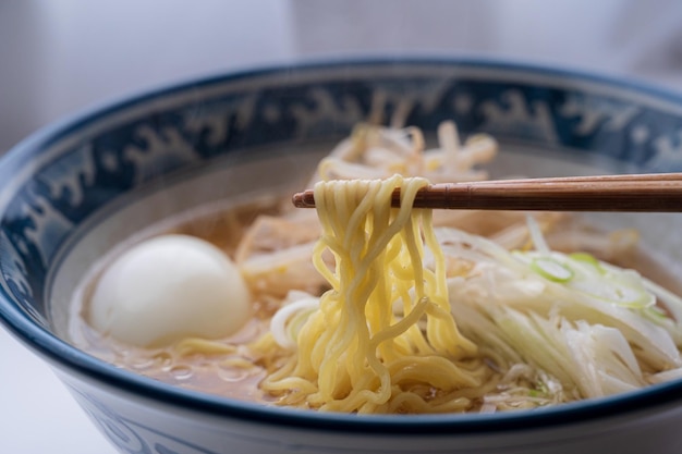 白い卵をスプーンで保持しているラーメンのボウル。