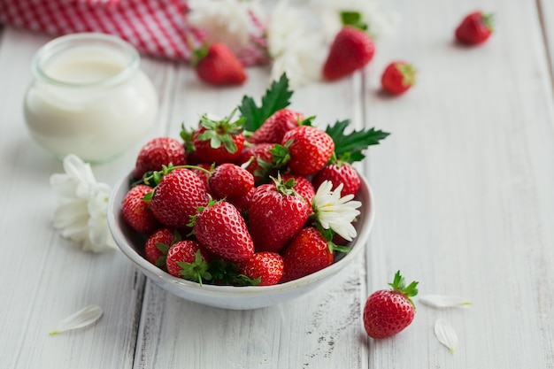 A bowl of red juicy strawberries on white wooden table. Healthy and diet snack food concept.