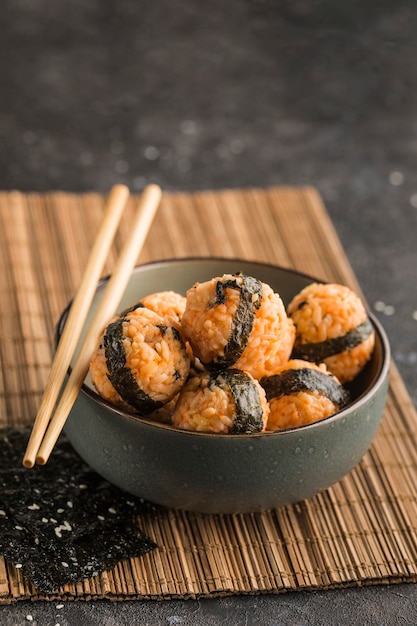 A bowl of rice balls with sesame seeds and nori seaweed, served with soy sauce, chopsticks on a dark background. Side view with a copy space. Vertical orientation