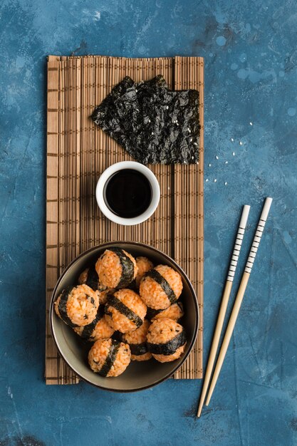 紺色の背景に醤油と箸を添えたごまと海苔の入ったおにぎり。コピースペースのある側面図。垂直方向