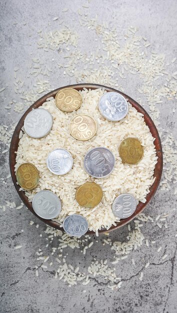 A bowl of rice and indonesian rupiah coins over cement textured background