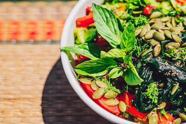 A bowl of salad green seeds pumpkin basil leaves tomato juice seaweed