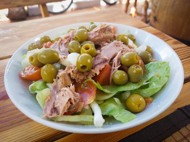 A bowl of salad with green olives and a piece of meat on top of it.