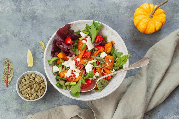 A bowl of salad with a spoon next to it and a bowl of feta.