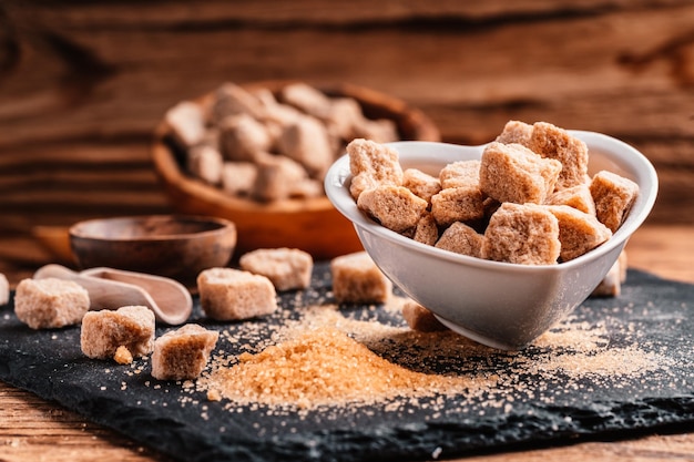 Bowl and scoop with sand and lump brown sugar on wooden\
background brown sugar cube make unhealthy nutrition obesity\
diabetes dental care and much more