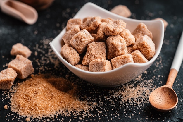 Bowl and scoop with sand and lump brown sugar on wooden background brown sugar cube Make unhealthy nutrition obesity diabetes dental care and much more