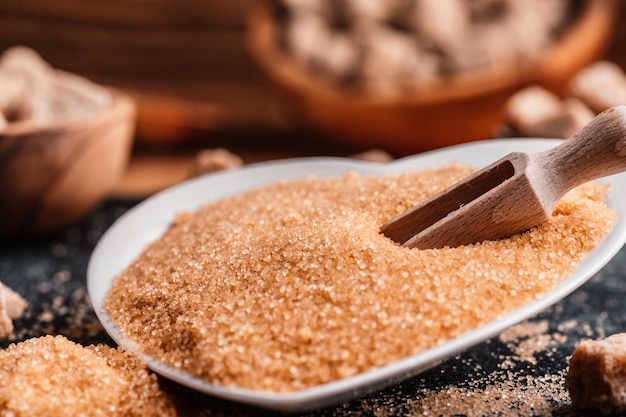 Bowl and scoop with sand and lump brown sugar on wooden\
background brown sugar cube make unhealthy nutrition obesity\
diabetes dental care and much more