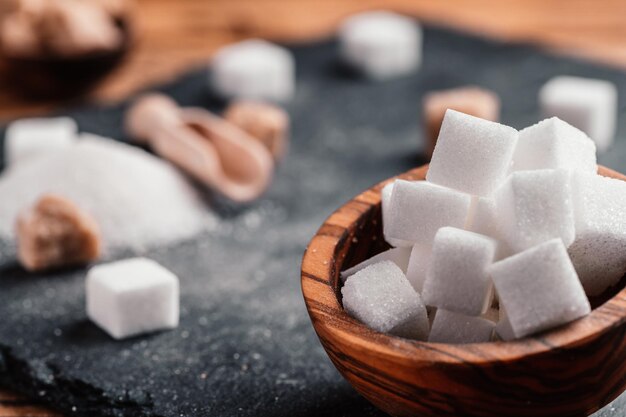 Bowl and scoop with white sand and lump white sugar on wooden
background sugar cube make unhealthy nutrition obesity diabetes
dental care and much more