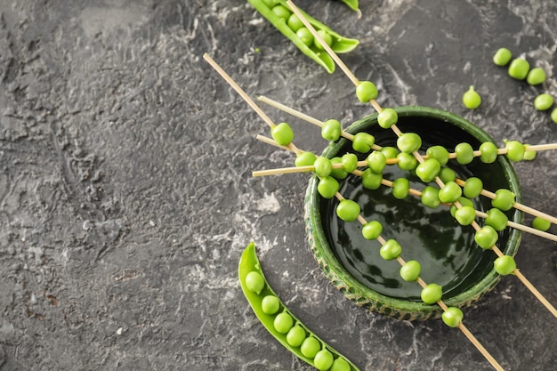 Bowl and skewers with fresh green peas on grey textured surface