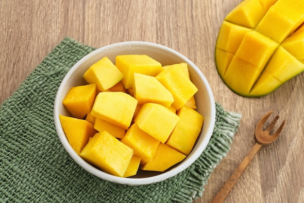 A bowl of sliced fresh mango cubes on wooden background.