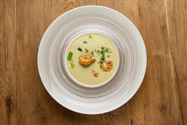 A bowl of soup with scallops on top of a wooden table
