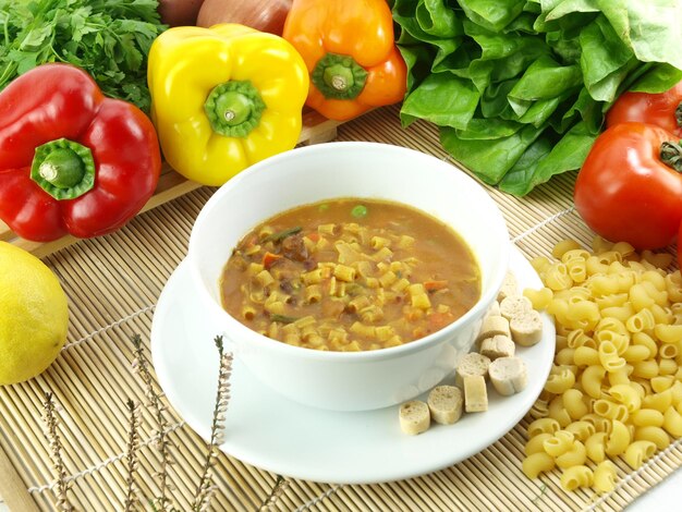 A bowl of soup with a variety of vegetables on a table.