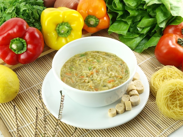 A bowl of soup with vegetables on a table next to it