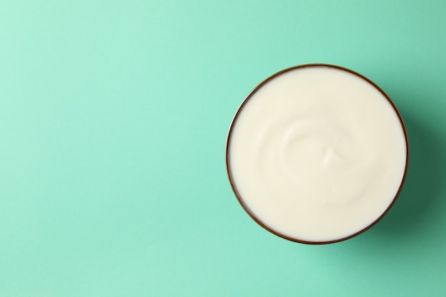 Bowl of sour cream on mint background, top view