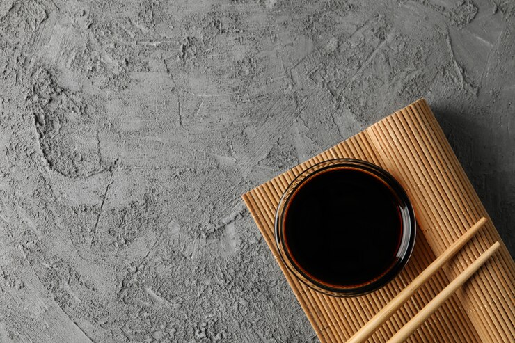 Photo bowl of soy sauce on gray background, space for text. top view