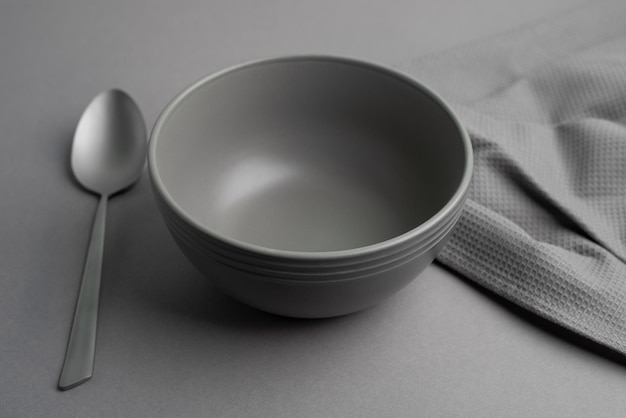 A bowl, a spoon and a kitchen towel on grey background. Table setting concept. Flat lay, top view.