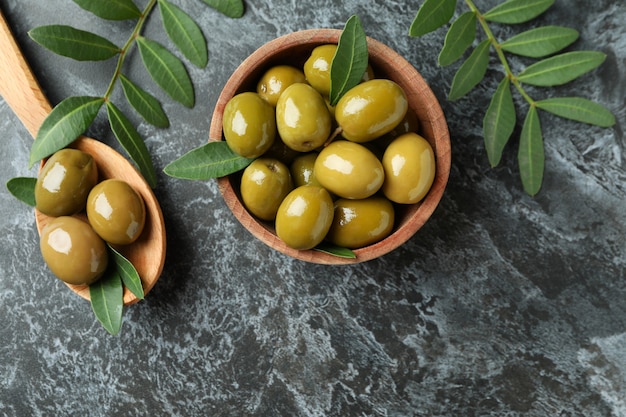 Bowl and spoon of olives, and leaves on black smokey background