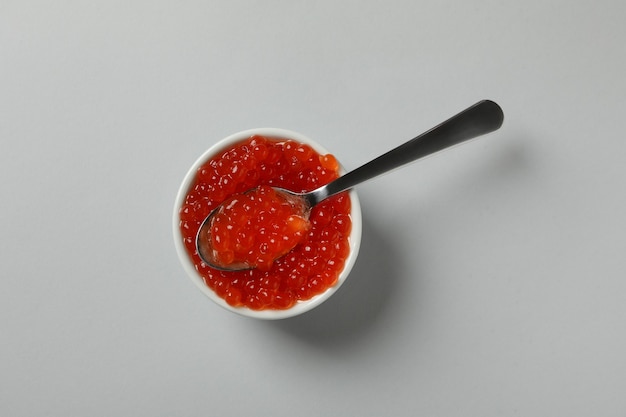 Bowl and spoon with caviar on gray background
