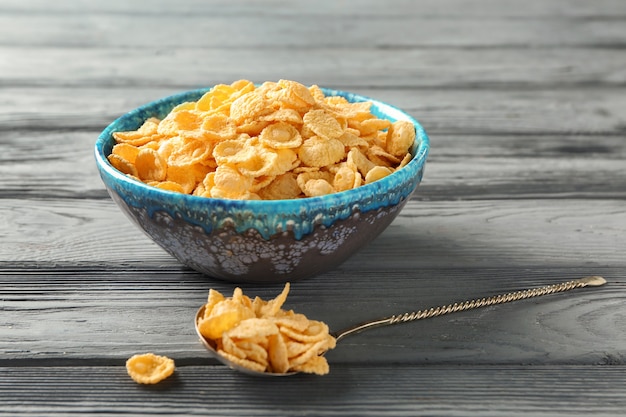 Bowl and spoon with tasty corn flakes on wooden