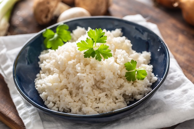 Bowl of steamed rice with mushrooms and leaks in the background.