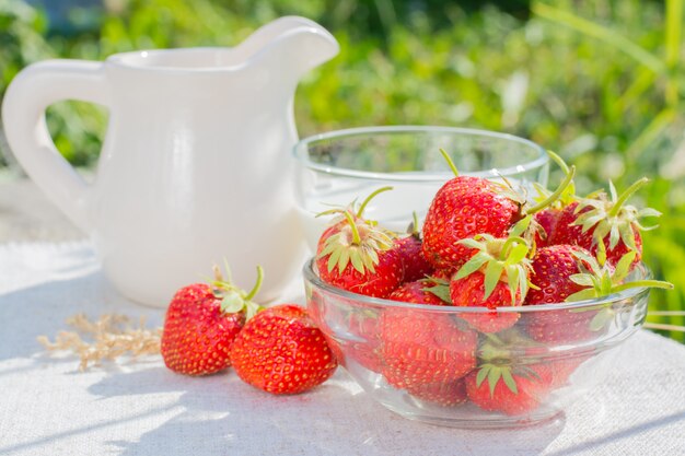 Una ciotola di fragole, una tazza di latte e una brocca su un tovagliolo su un tavolo di legno