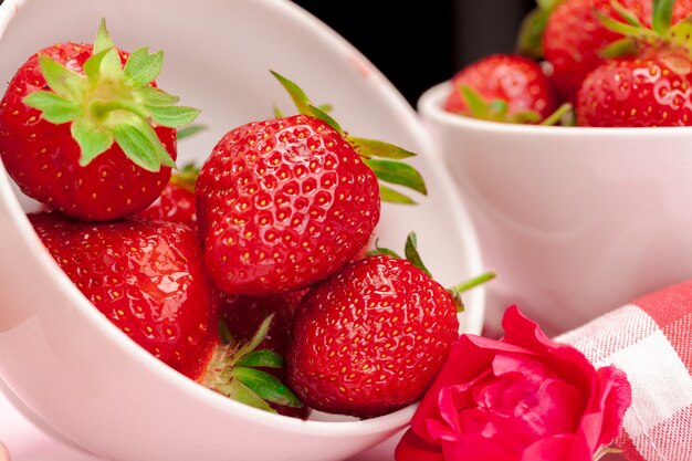 Bowl of strawberry harvest on wooden table close up