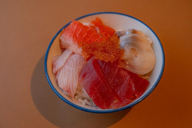 A bowl of sushi with a white bowl of salmon and oysters.