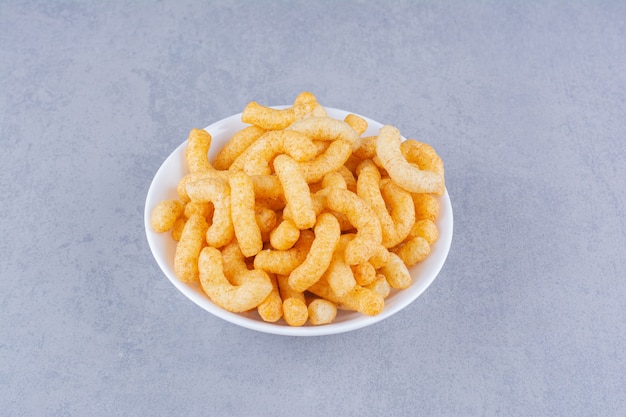 A bowl of tasty corn sticks on the marble surface