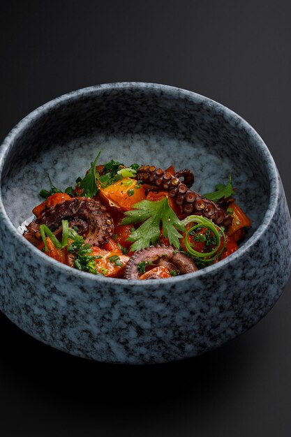 Bowl of tentacles of the octopus with grilled vegetables isolated over black background