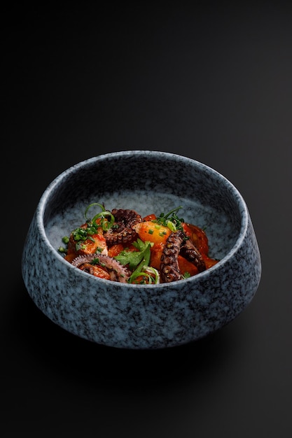 Bowl of tentacles of the octopus with grilled vegetables isolated over black background