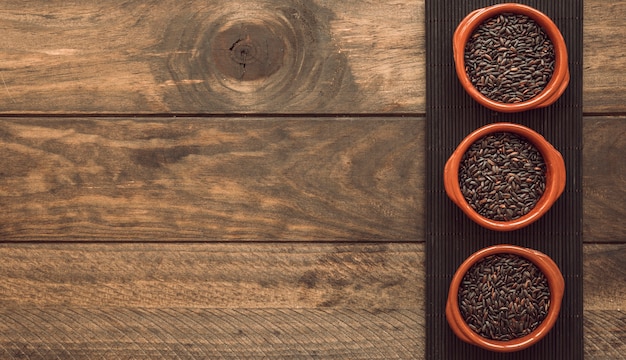 Photo bowl of three bowls with brown rice on tray over the wooden table