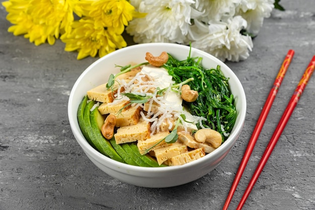 Photo a bowl of tofu with a white bowl of spinach and a pair of red flowers behind it.