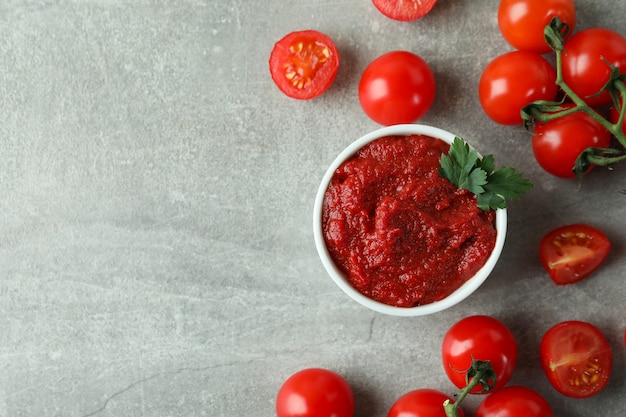 Ciotola di concentrato di pomodoro e pomodori su grigio testurizzato