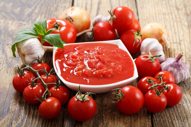 Bowl of tomato sauce with fresh vegetables on wooden table