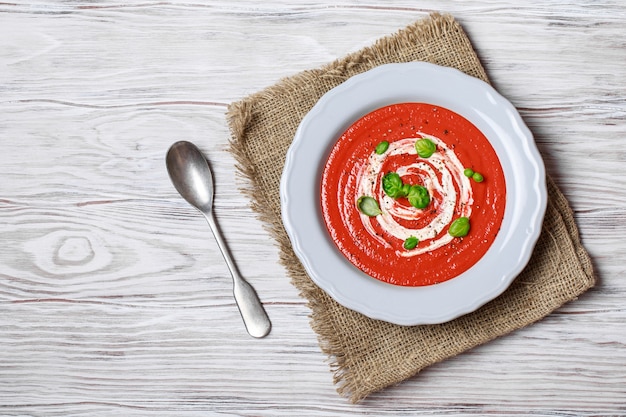 Bowl of tomato soup with a basil on wooden background