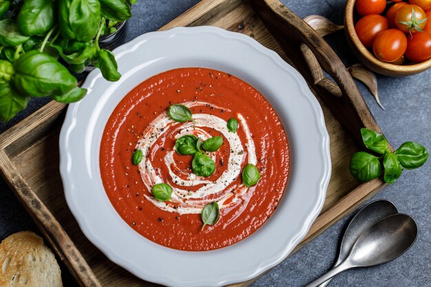 Bowl of tomato soup with a basil on wooden background