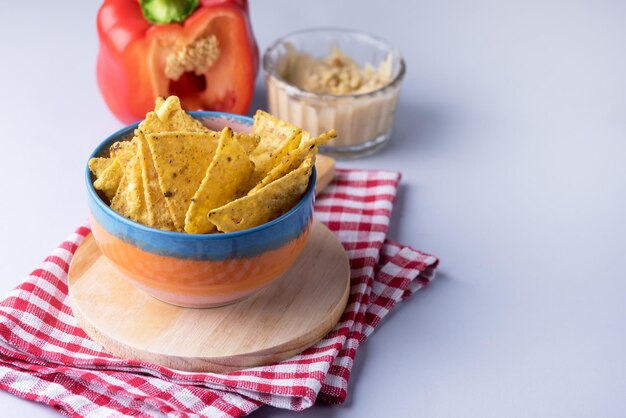 Bowl of Tortilla or Corn Chips on Wooden Tray Bowl with Himmus Copy Space Blue Background Horizontal