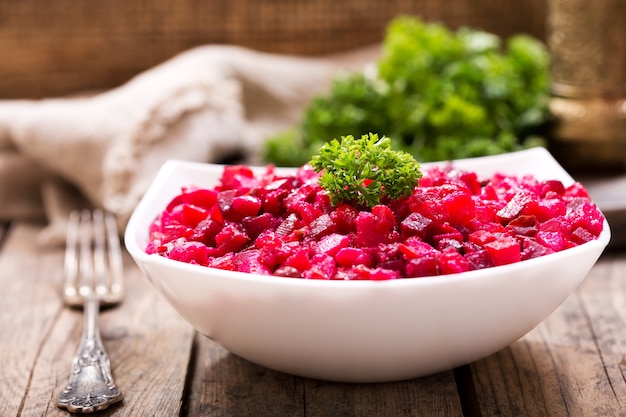 Bowl of traditional russian beet salad vinaigrette on wooden table
