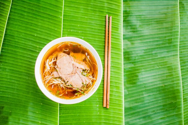 bowl of Traditional Vietnamese beef soup Pho Bo on banana leaf background.