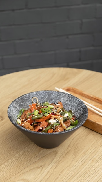 A bowl of udon noodles veal and fried vegetables angle view on wooden table