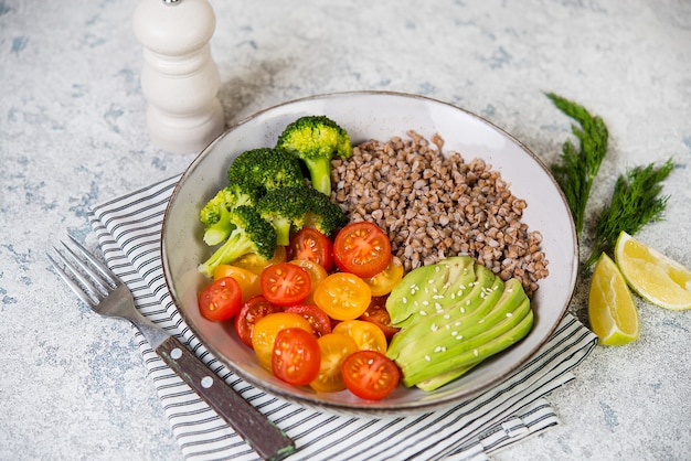 A bowl of vegan food, a vegan dinner of boiled buckwheat, colored tomatoes, avocado and broccoli. Top view, selective focus