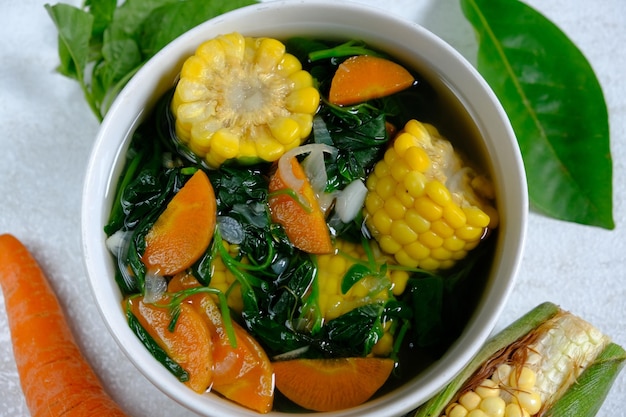 A bowl of vegetable soup with a green leaf next to it