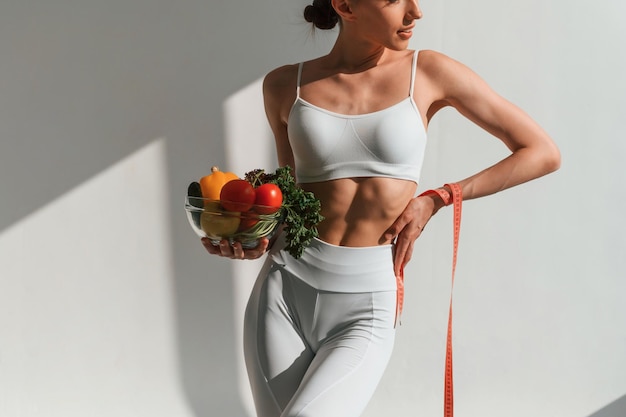 Photo bowl of vegetables and fruits young caucasian woman with slim body shape is indoors in the studio