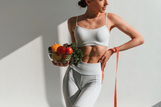 bowl of vegetables and fruits Young caucasian woman with slim body shape is indoors in the studio