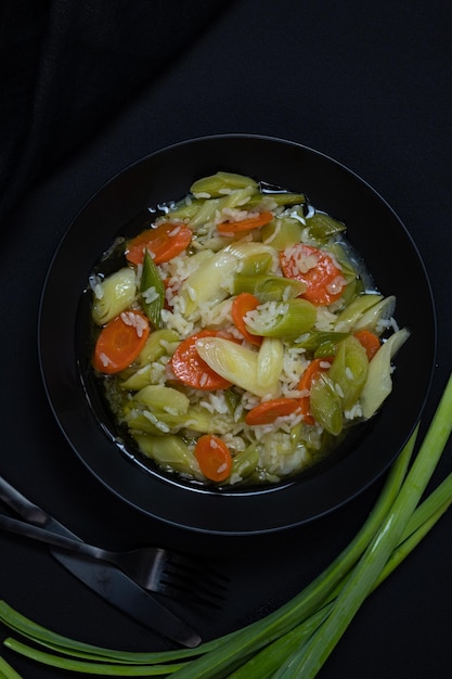 A bowl of vegetables and rice with a green onion on the side.