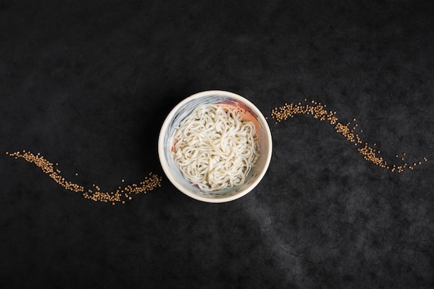 Bowl of white noodles decorated with coriander seeds on black backdrop