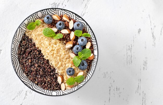 Bowl of white, red and black cooked quinoa with nuts and blueberries