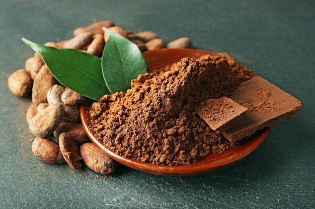 Bowl with aromatic cocoa beans and chocolate on grey background close up