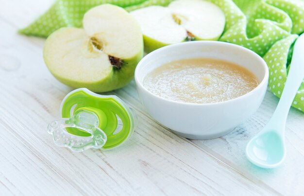 Bowl with baby food and apples on table